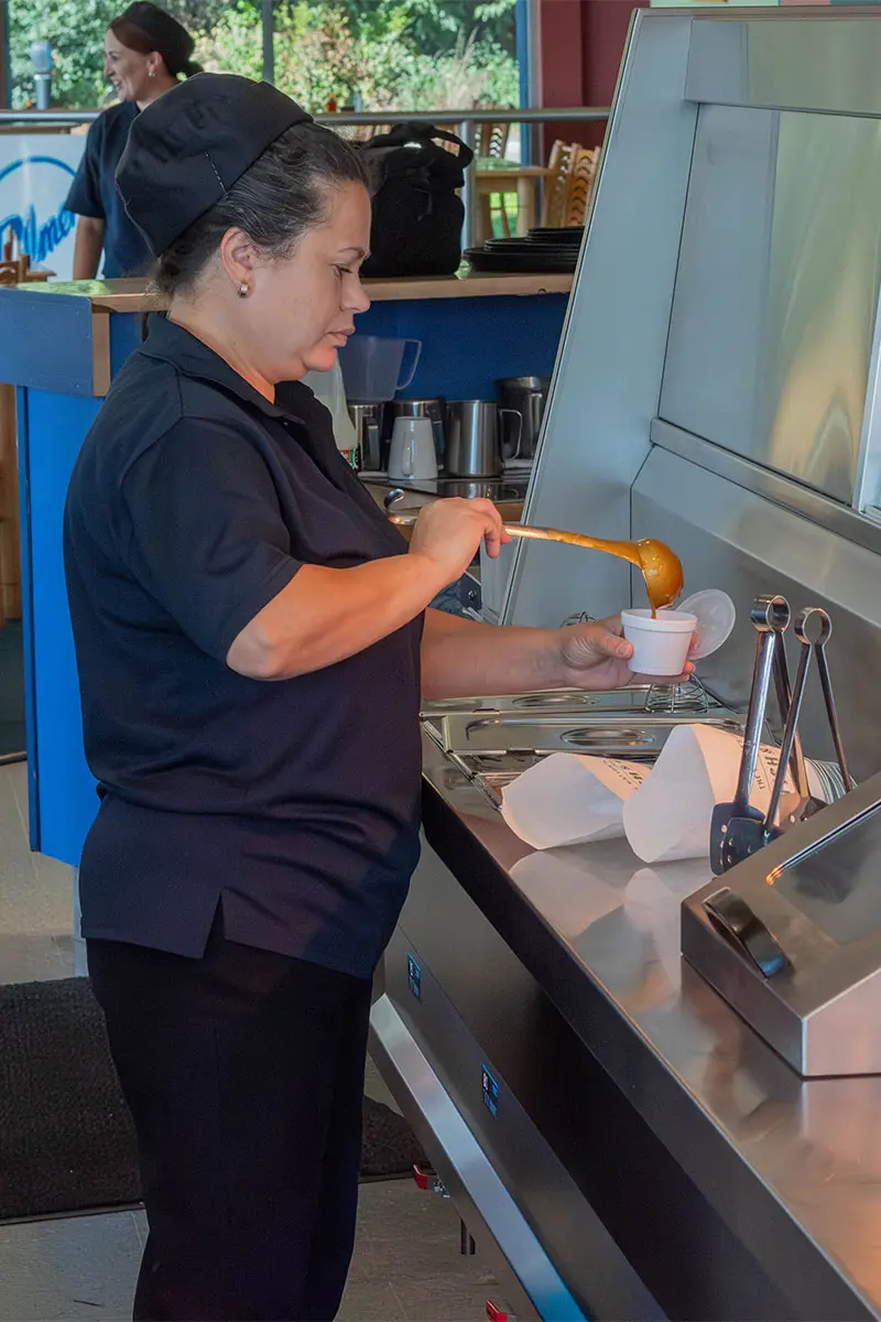 Staff member in Palmers Fish and Chips, pouring curry sauce into a polystyrene container using a ladle