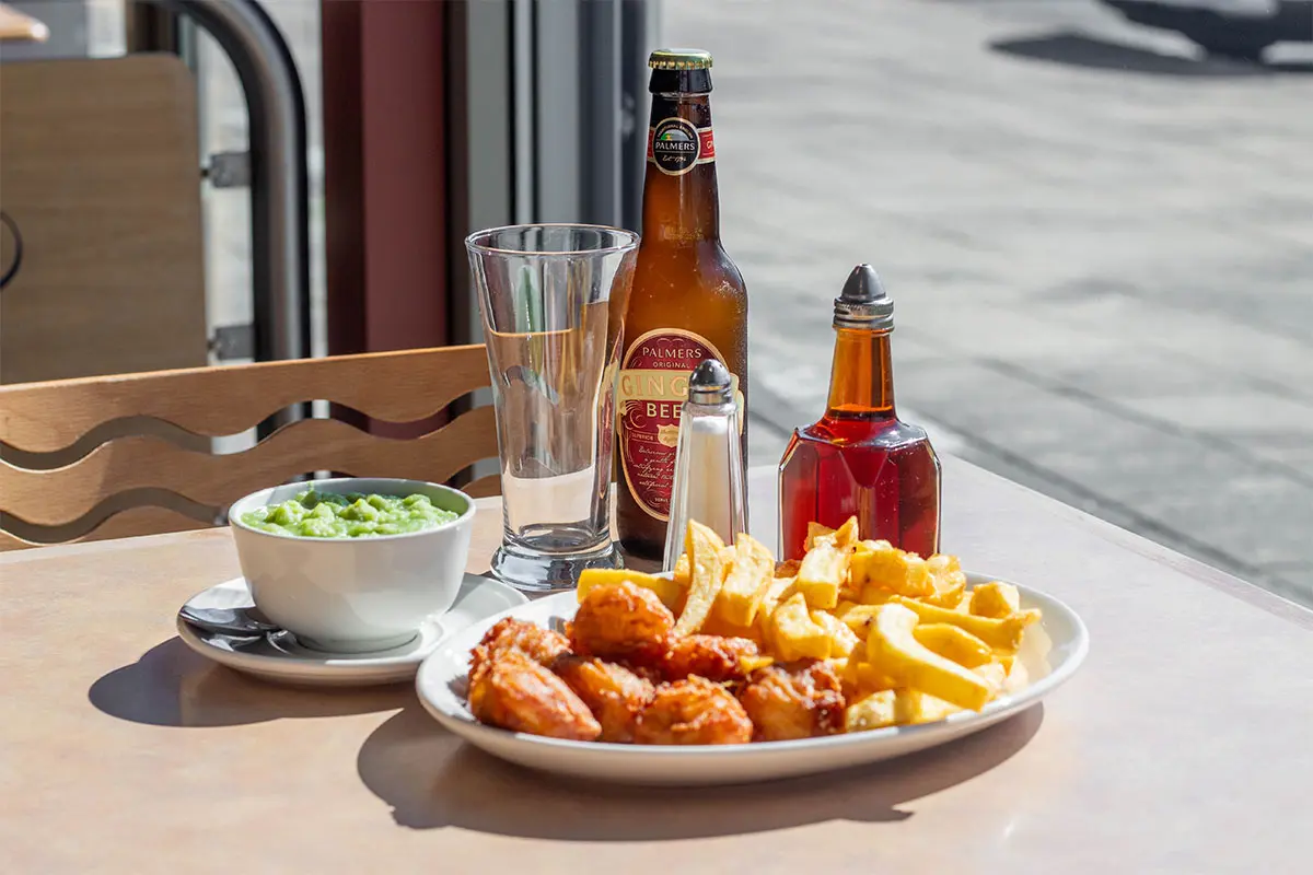 Chicken nuggets and chips on a plate with a bowl of mushy peas and a bottle of ginger beer at Palmers fish and chips restaurant