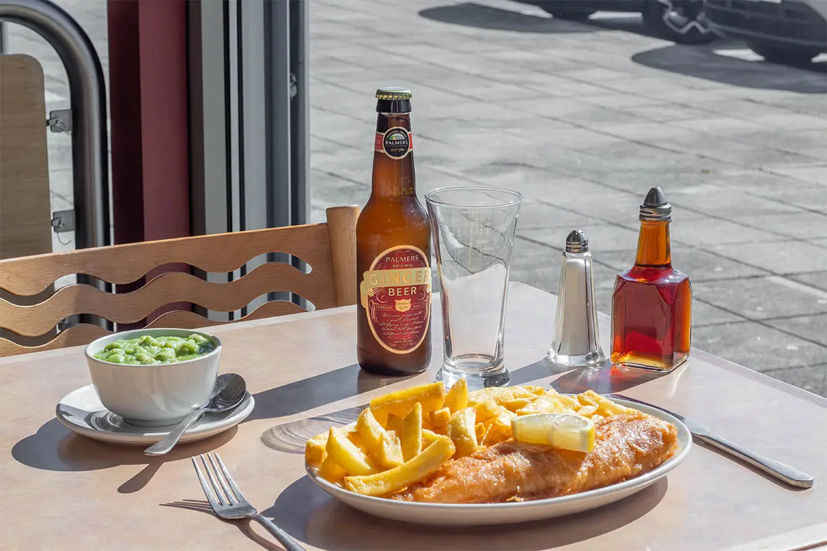 Fish and chips on a plate, with a bowl of mushy peas and a bottle of Palmers original Ginger Beer on the table in the Palmers Fish and Chips Restaurant