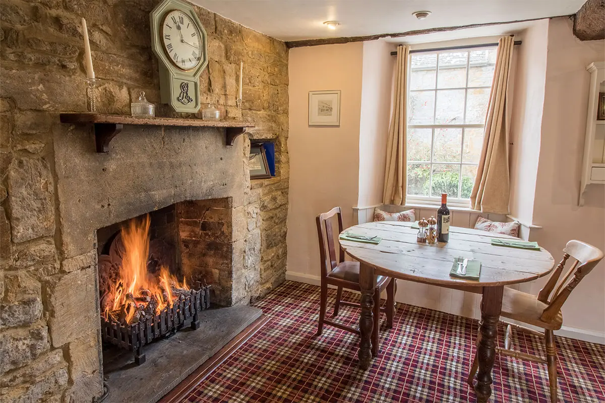 Inside The Royal Oak Over Stratton restaurant with a table set up for customers and a roaring fire beside