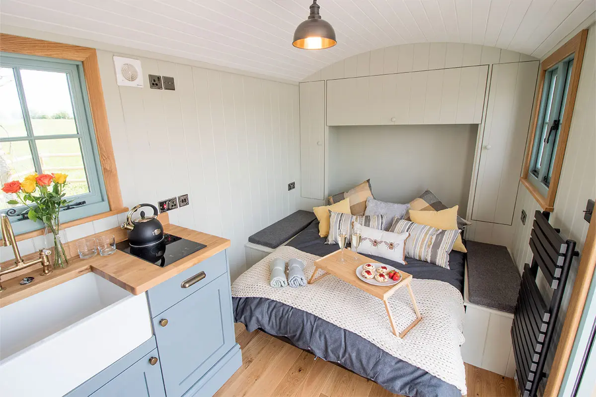 Bed with a small table with scones, strawberries and champagne on it, in a shepherds hut