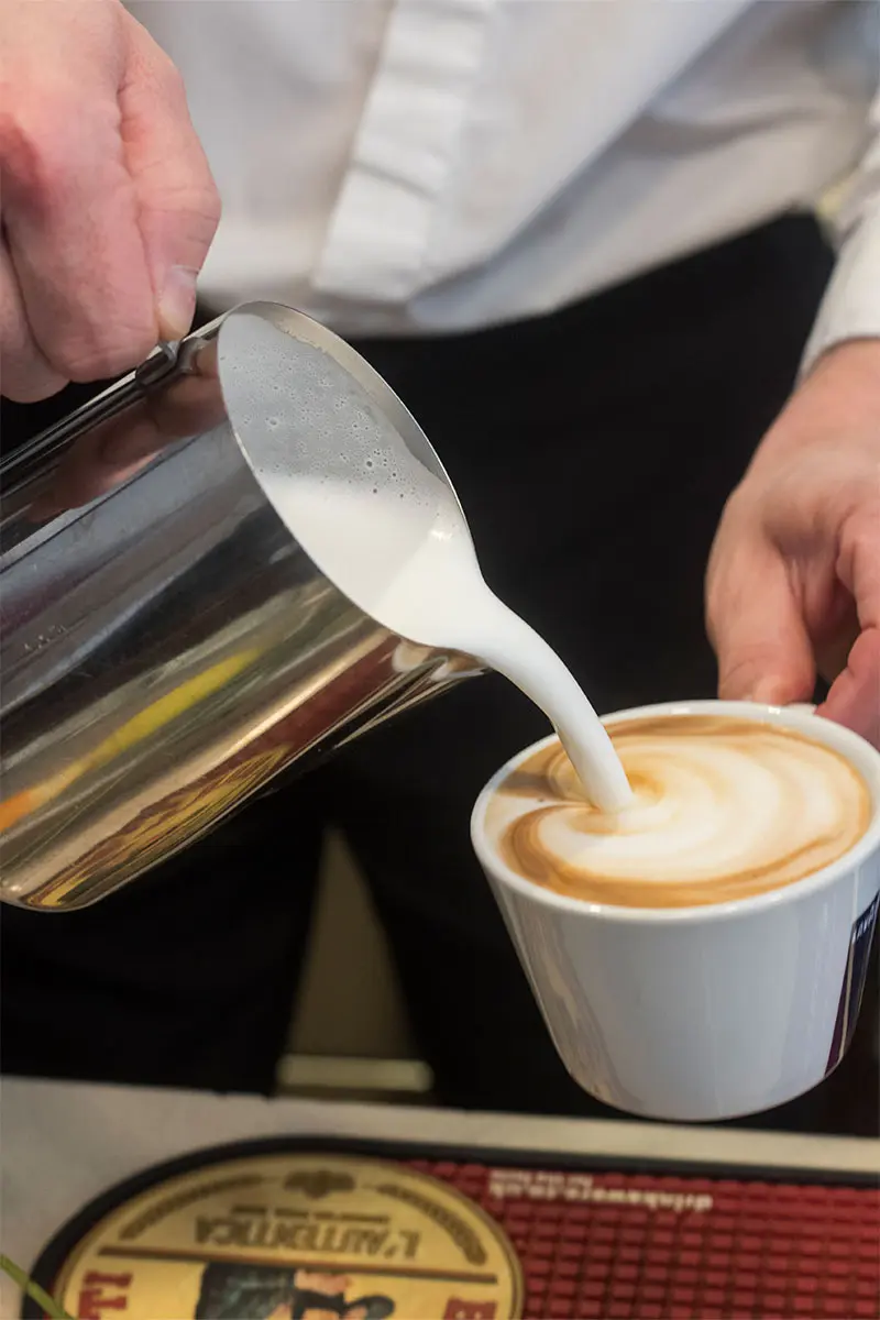 Tamburinos waiter pouring milk into a cup of coffee